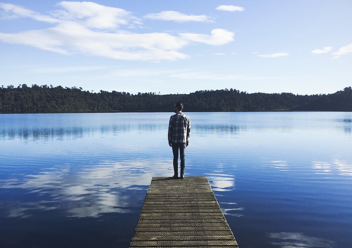 man standing on a pier, looking out over a lake