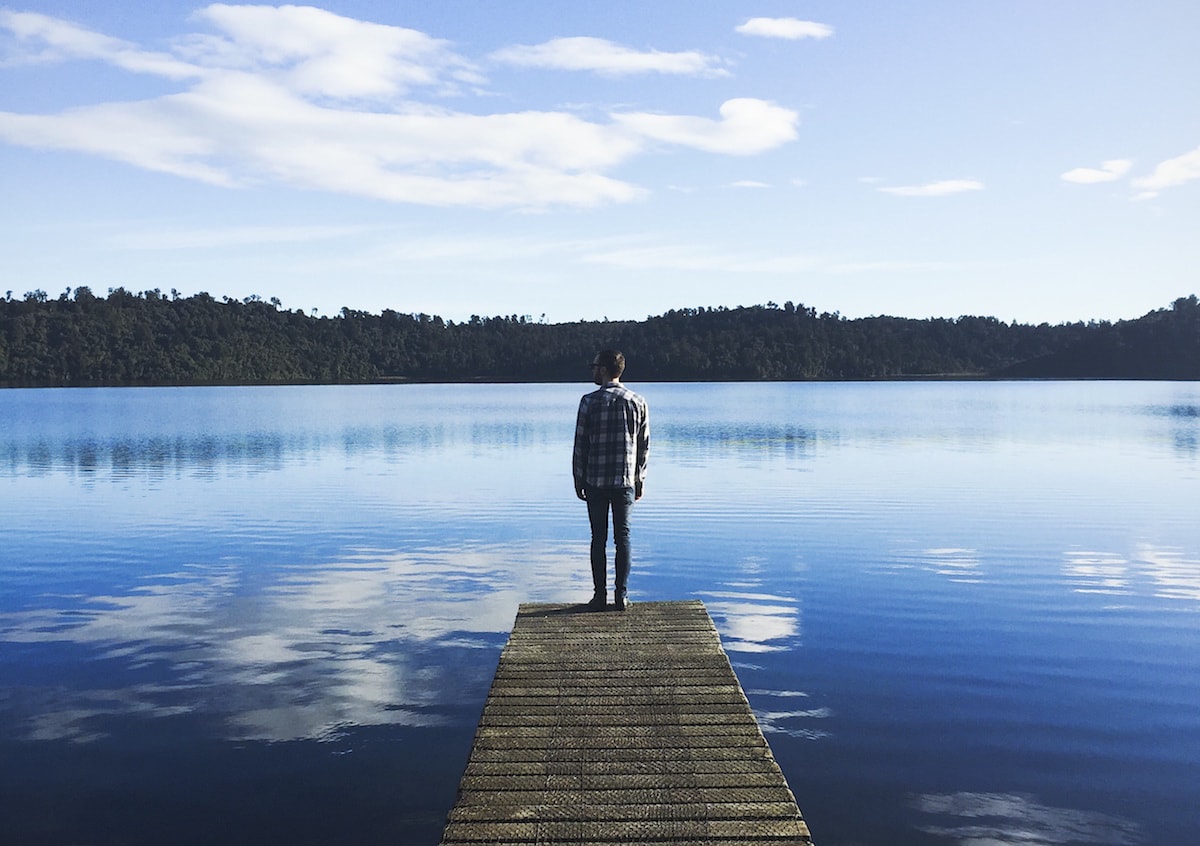man standing on a pier, looking out over a lake